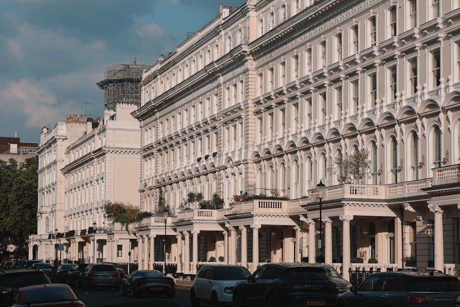 Street view of elegant white Victorian terrace houses in Clapham SW4, featuring ornate architectural details, bay windows, decorative moldings, and balconies with potted plants. The pavement is lined with a row of parked cars, and the buildings are illuminated by daylight under a partly cloudy sky. The scene showcases well-maintained facades with clean surfaces, reflecting high standards of property upkeep, consistent with professional domestic and commercial cleaning standards offered by Clapham Carpet Cleaning. The image emphasizes the architectural beauty of Victorian flats in Clapham, highlighting surfaces and features associated with deep cleaning and surface sanitisation.